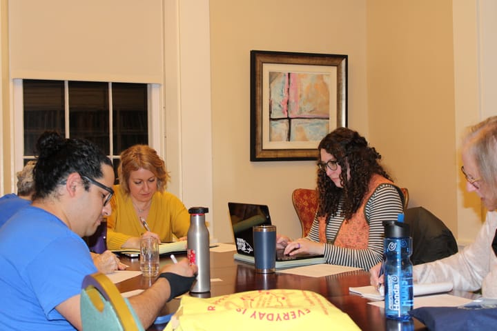 Several people sit around a table and write on pieces of paper