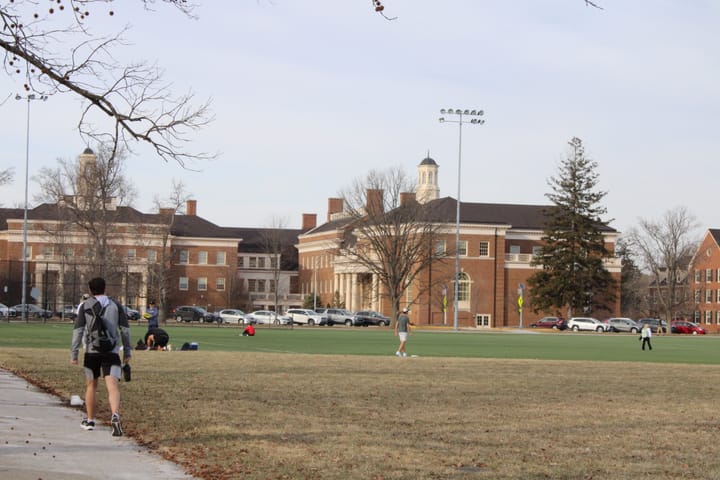 Groups of students stand on Cook Field in front of the Farmer School of Business