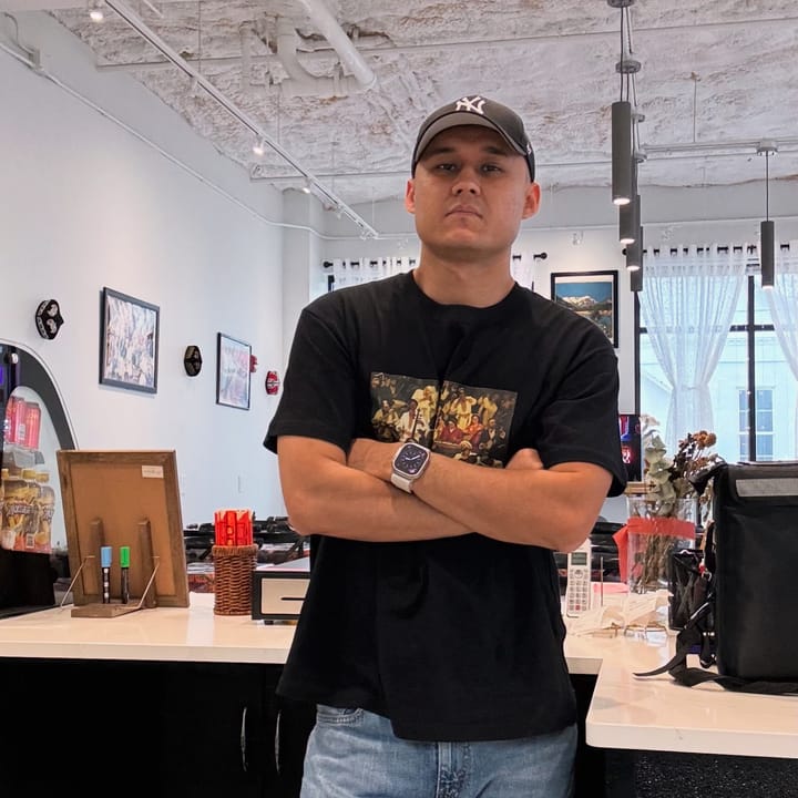 Daniel Kudusi stands with arms folded in front of a counter