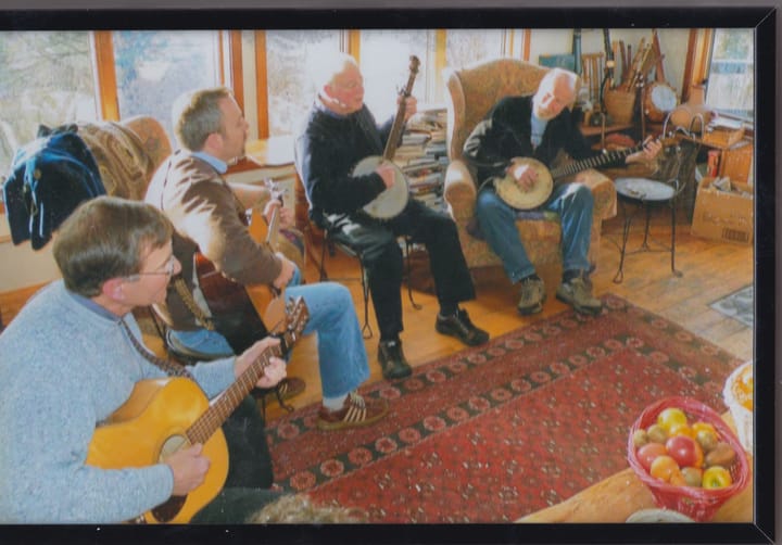 Four men sit playing guitar and banjo in a sunroom