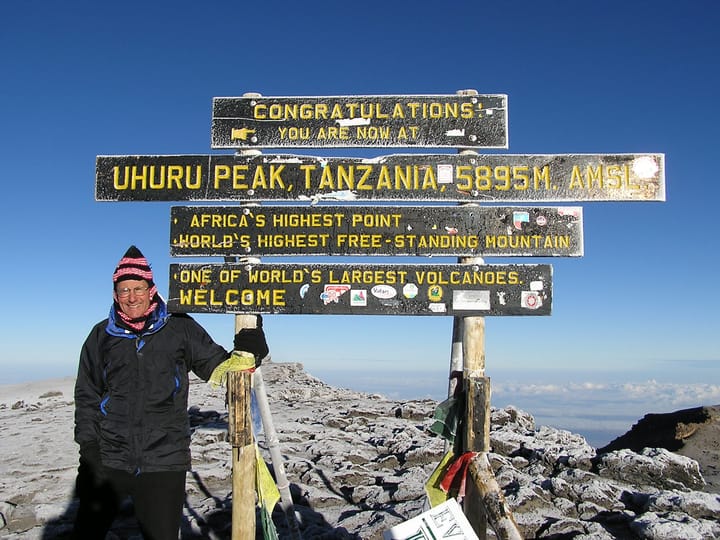 Allan Winkler stands next to a sign at the summit of Mount Kilimanjaro