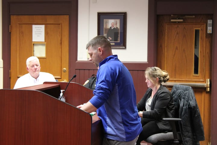 Casey Wooddell speaks at a podium, facing left